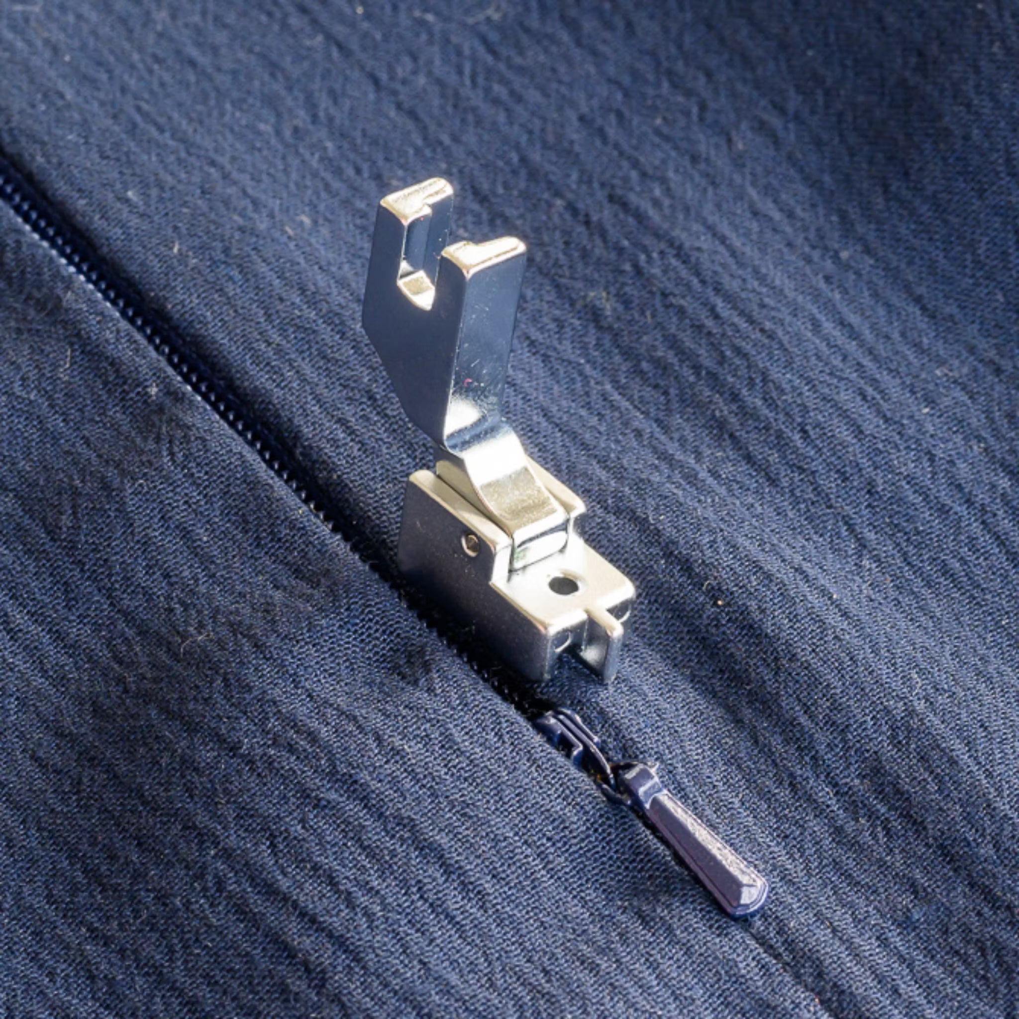 Metal sewing machine zipper foot on a blue fabric background